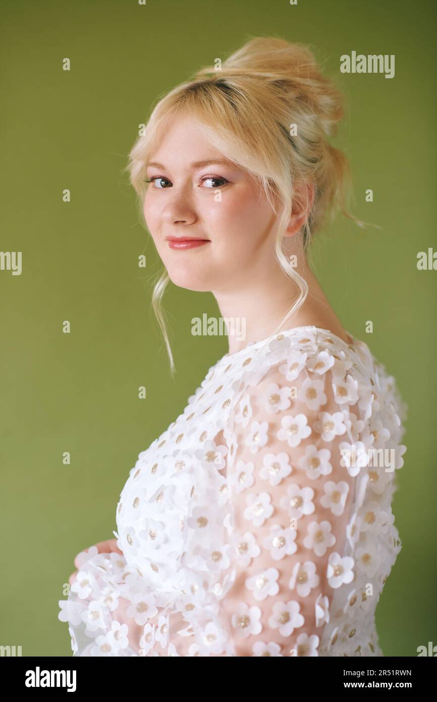 Schönheitsportrait eines hübschen jungen 15 - 16 Jahre alten Teenager-Mädchens, das ein weißes Kleid trägt und auf grünem Hintergrund posiert Stockfoto