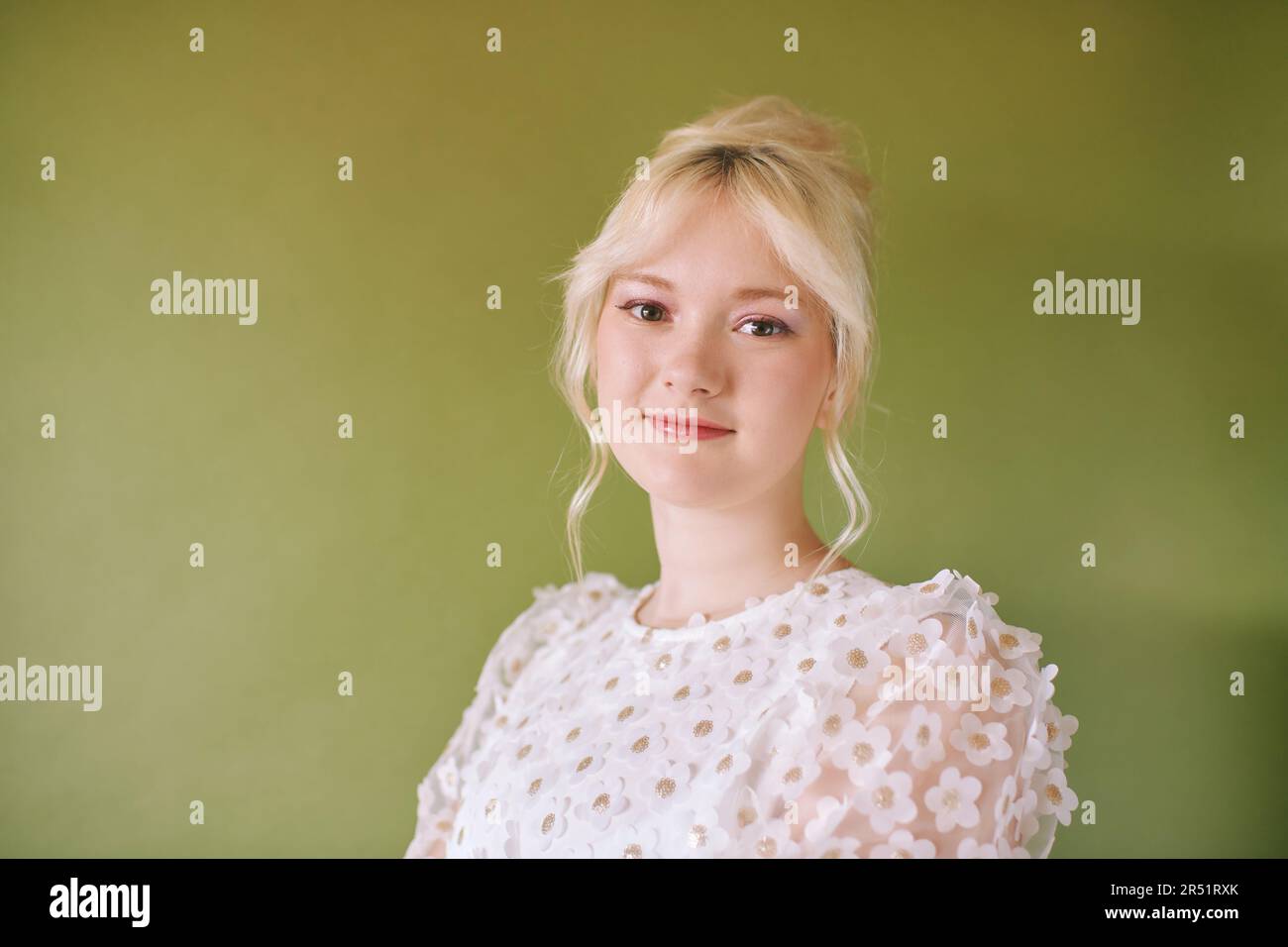 Schönheitsportrait eines hübschen jungen 15 - 16 Jahre alten Teenager-Mädchens, das ein weißes Kleid trägt und auf grünem Hintergrund posiert Stockfoto
