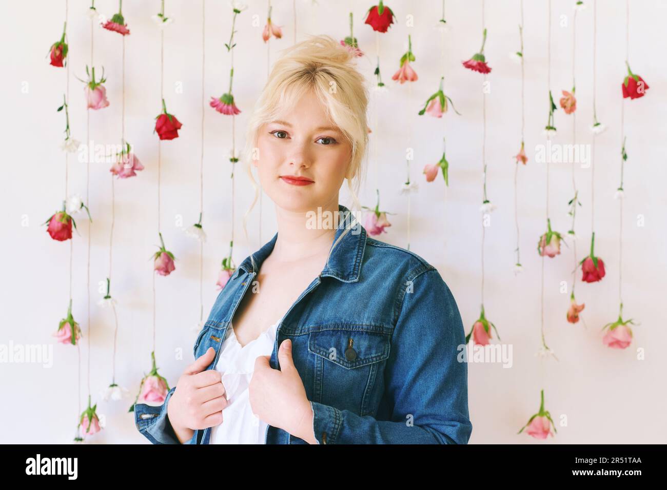 Studioporträt eines hübschen jungen Mädchens im Alter von 15 bis 16 Jahren, das eine Jeansjacke trägt und auf weißem Hintergrund mit hängenden Blumen, Schönheit und Mode posiert Stockfoto