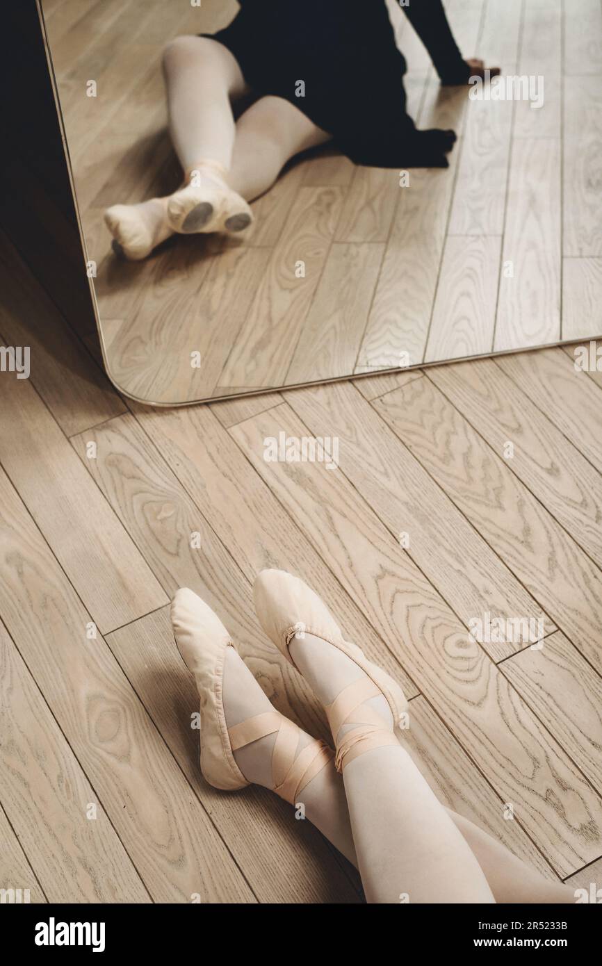 Großer Winkel einer nicht erkennbaren Balletttänzerin, die auf dem Boden in pointe-Schuhen vor dem Spiegel sitzt, während sie sich während der Probe im Studio ausruht Stockfoto