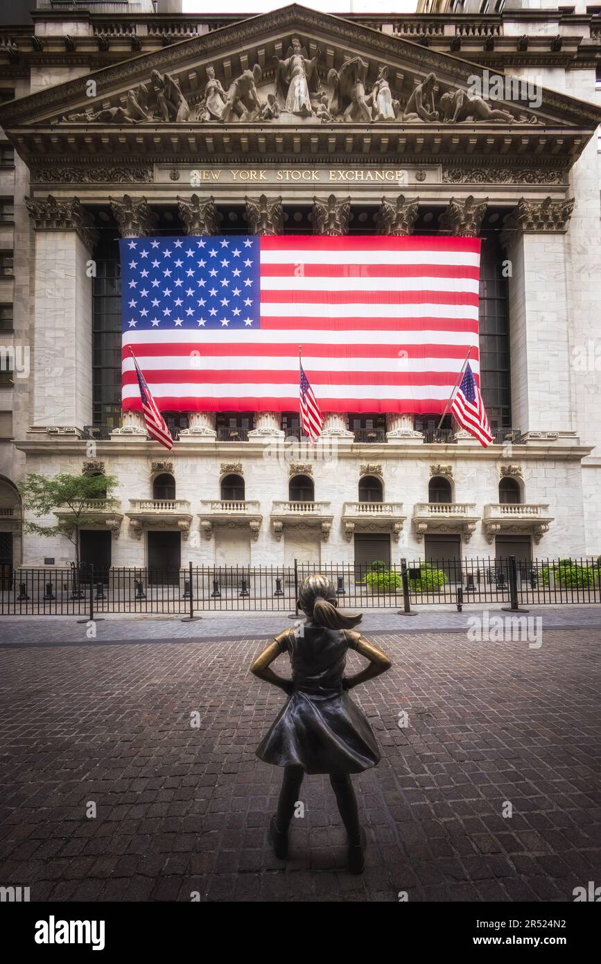 Wall Street Fearless Girl - die New Yorker Börse mit der großen amerikanischen Flagge und dem Fearless Statue Girl im Vordergrund. Dieses Bild ist al Stockfoto