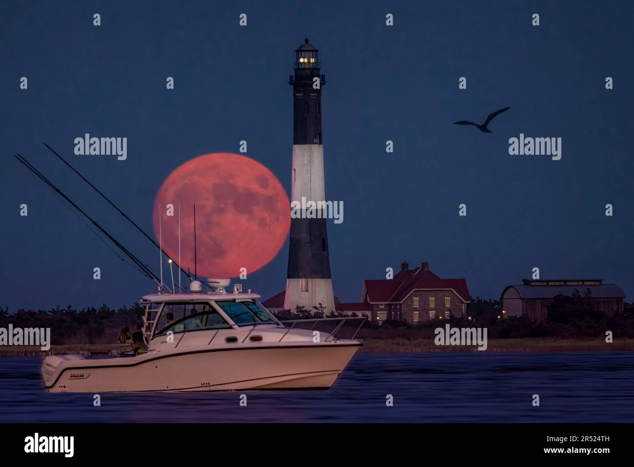 Fire Island Lighthouse Moon - der Vollerntmond erhebt sich hinter dem Fire Island Lighthouse und einem Freizeitboot in der Bucht. Fire Island Leuchtturm i Stockfoto