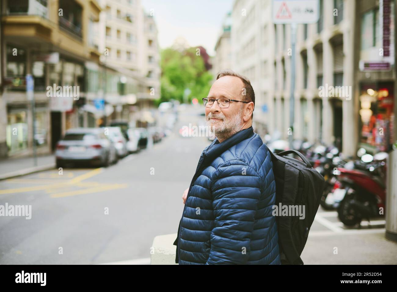 Außenporträt eines 55-60-jährigen Mannes mit blauer Jacke und Rucksack mit Blick über die Schulter Stockfoto