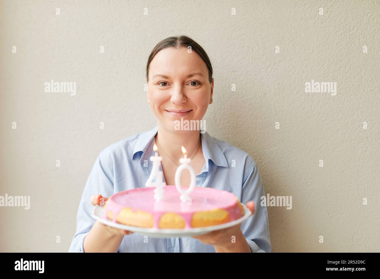 Glückliche 40-jährige Frau, die Kuchen mit Kerzen hält Stockfoto