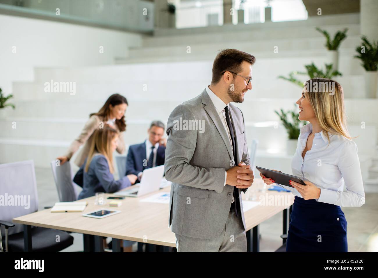 Attraktives junges Geschäftspaar, das sich die finanziellen Ergebnisse auf einem digitalen Tablet vor seinem Team im Büro ansieht Stockfoto