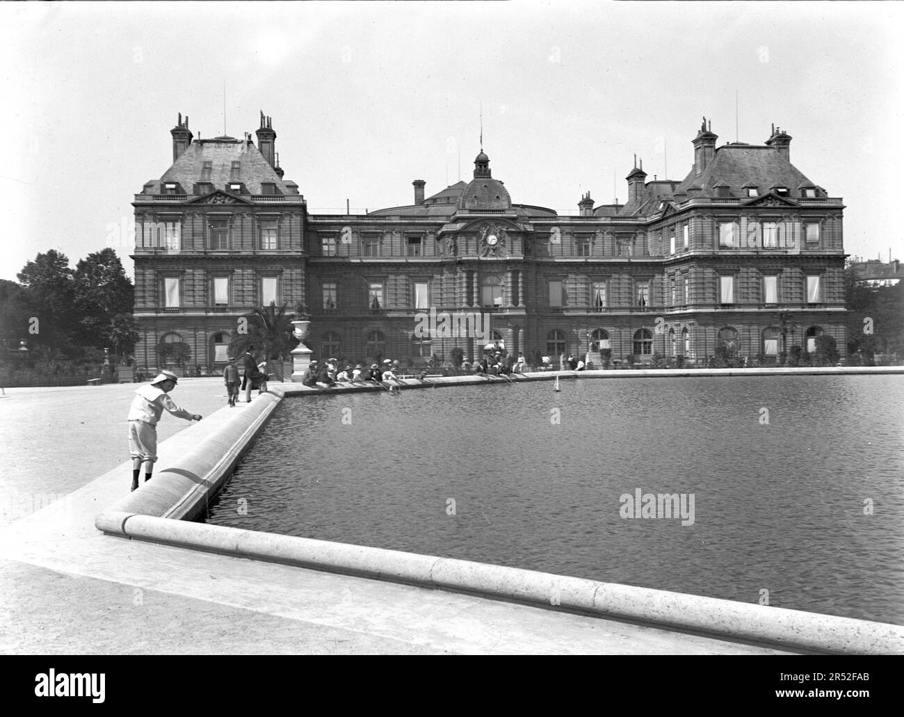 Ein Kind im Matrosenkostüm spielt im Jardin von Luxemburg. Gut gekleidete Leute im Hintergrund. Anfang des 20. Jahrhunderts. Altes Foto. Stockfoto