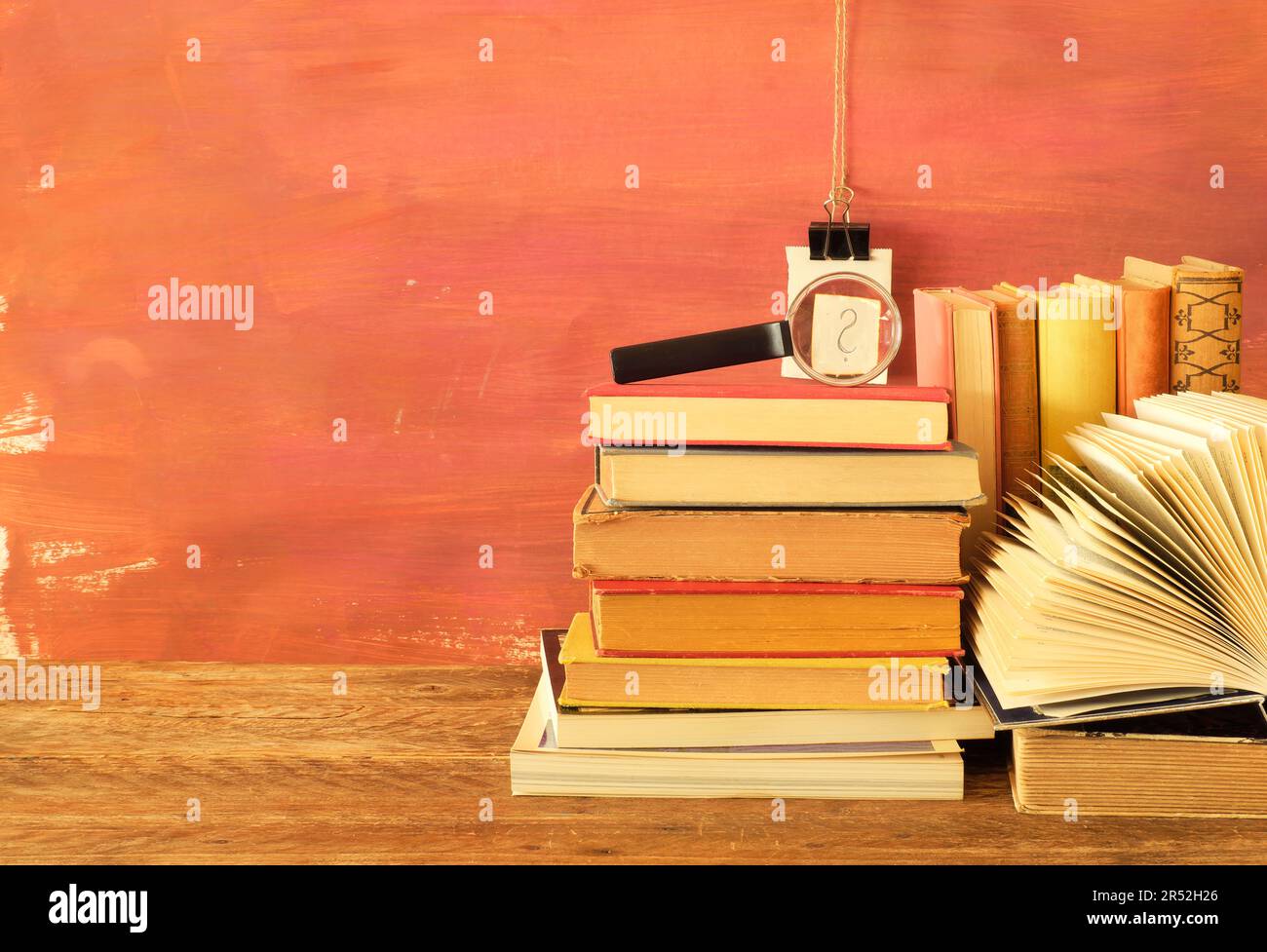 Bücherstapel, offenes Buch und Lupe mit Fragezeichen, Lernkonzept mit kostenlosem Kopierbereich Stockfoto