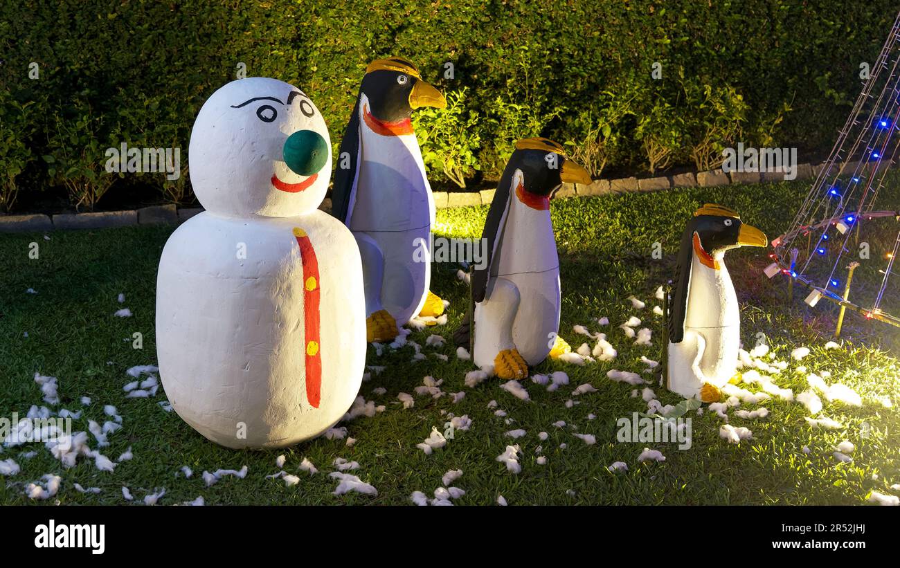 Gruselige beleuchtete Skulpturen von Pinguinen und ein Schneemann auf dem Rasen, was eine unheimliche und unkonventionelle Nachtszene schafft. Stockfoto