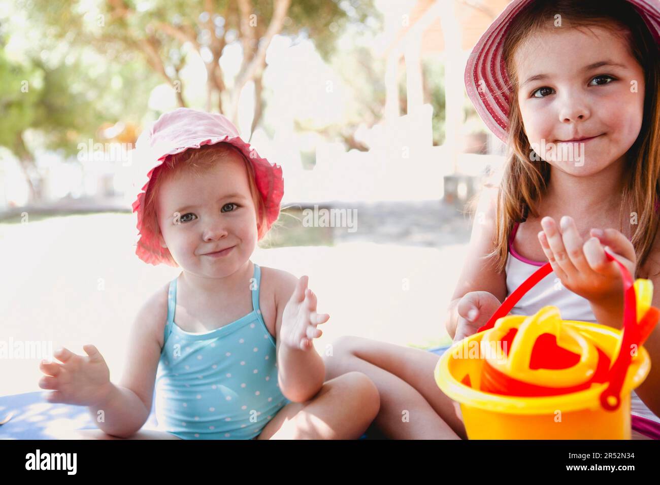 Liebenswert Schwestern im Sommer tragen sitzen im Schatten am Ufer Und mit Plastikspielzeug spielen Stockfoto