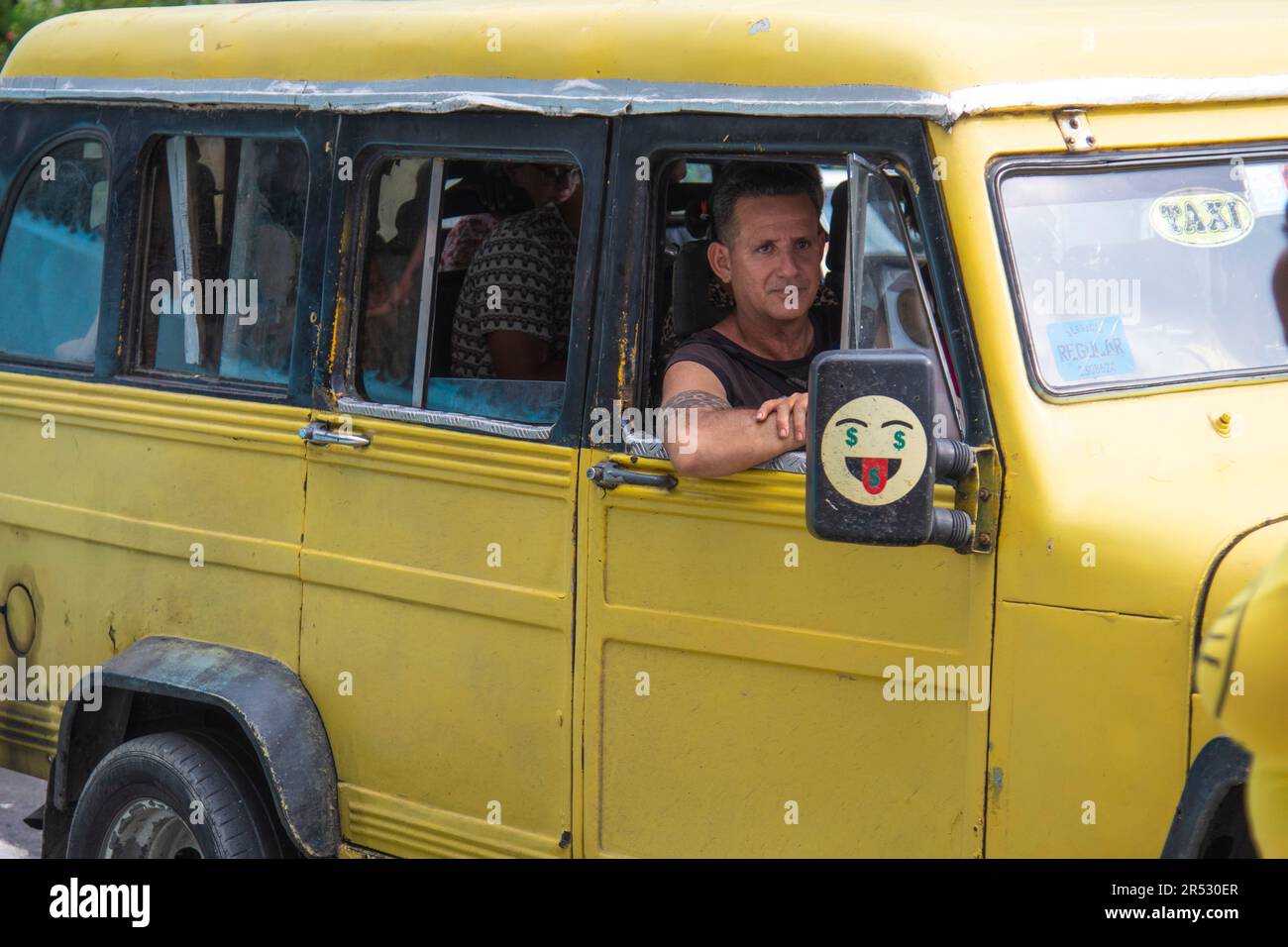 Der Passagier in einem kubanischen Taxi schaut aus dem Fenster und lächelt, während das Taxi die Straße in Havanna, Kuba, hinunter fährt. Stockfoto