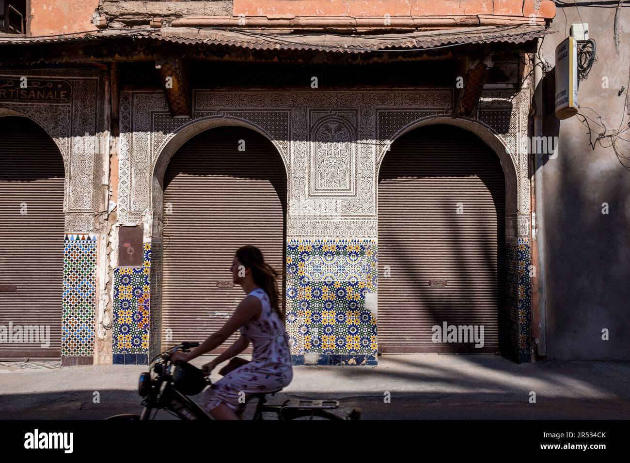 Eine Frau radelt an einer verfallenen Fassade in der Altstadt von Marrakesch, Marokko vorbei Stockfoto