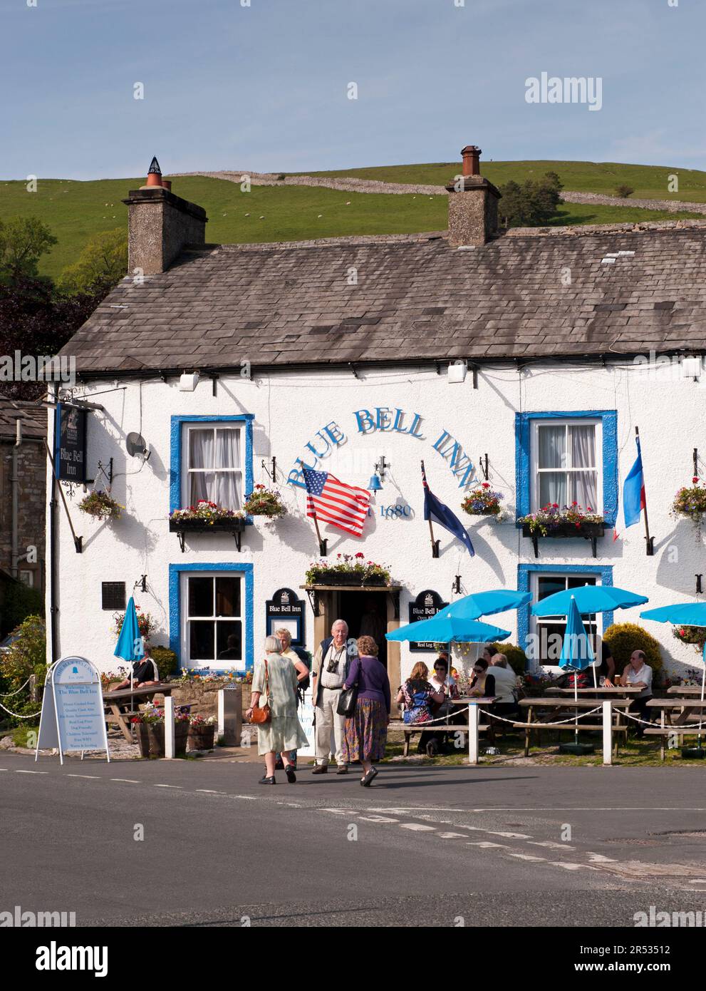 Gäste können sich unter Sonnenschirmen im malerischen Dorf Blue Bell Inn, Kettlewell, North Yorkshire, England, unterhalten und Getränke im Freien genießen. Stockfoto