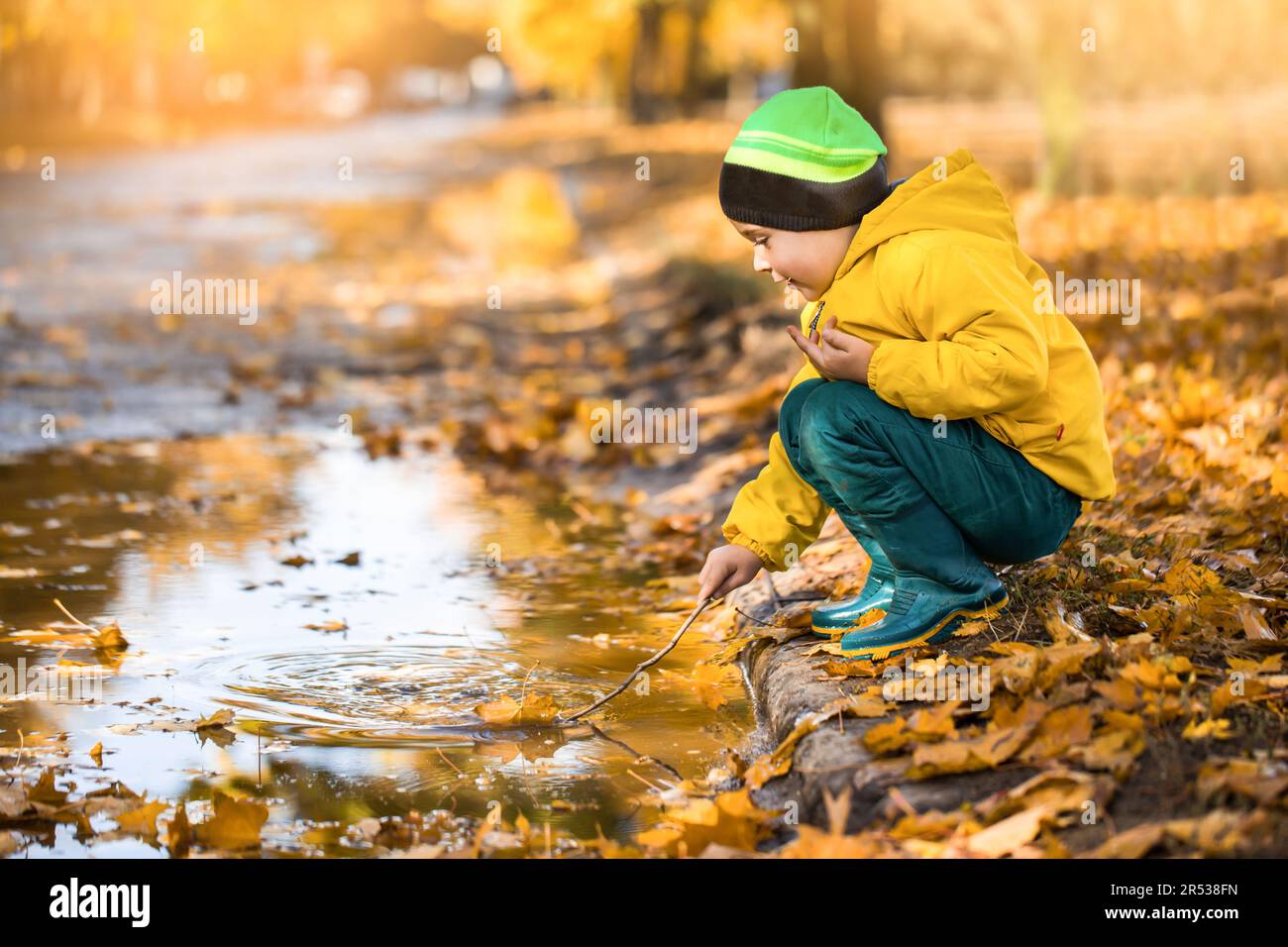 Der Junge im Herbstpark hat Spaß. Kleinkind wandert im Spätherbst und bei schlechtem Wetter durch die ländliche Landschaft Stockfoto