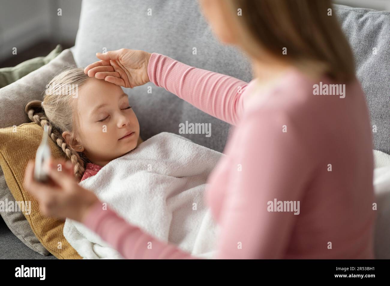 Hohes Fieber. Mom Überprüft Die Temperatur Ihrer Kranken Tochter, Die Auf Der Couch Schläft Stockfoto