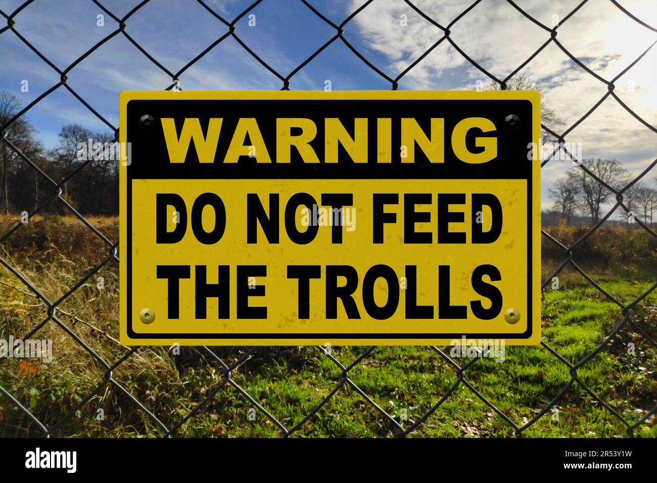 Schwarzes und gelbes Warnschild an einem Zaun mit der Aufschrift „Warnung - Trolle nicht füttern“. Stockfoto