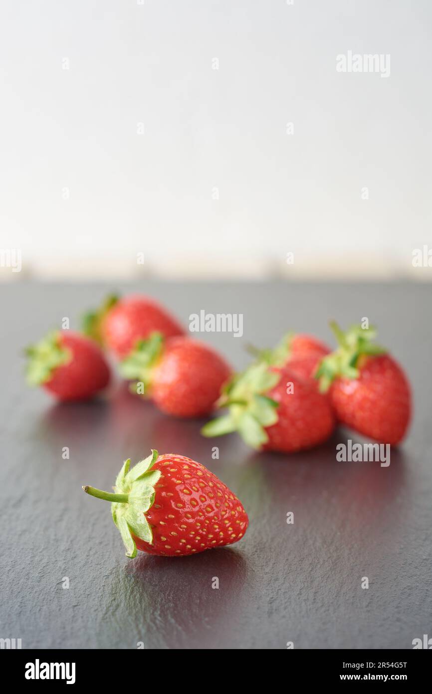 Seitenansicht frischer Erdbeeren auf schwarz strukturierter Oberfläche, hellrote Farbe beliebte saftige Früchte mit süßem Geschmack und duftendem Aroma, gesund Stockfoto