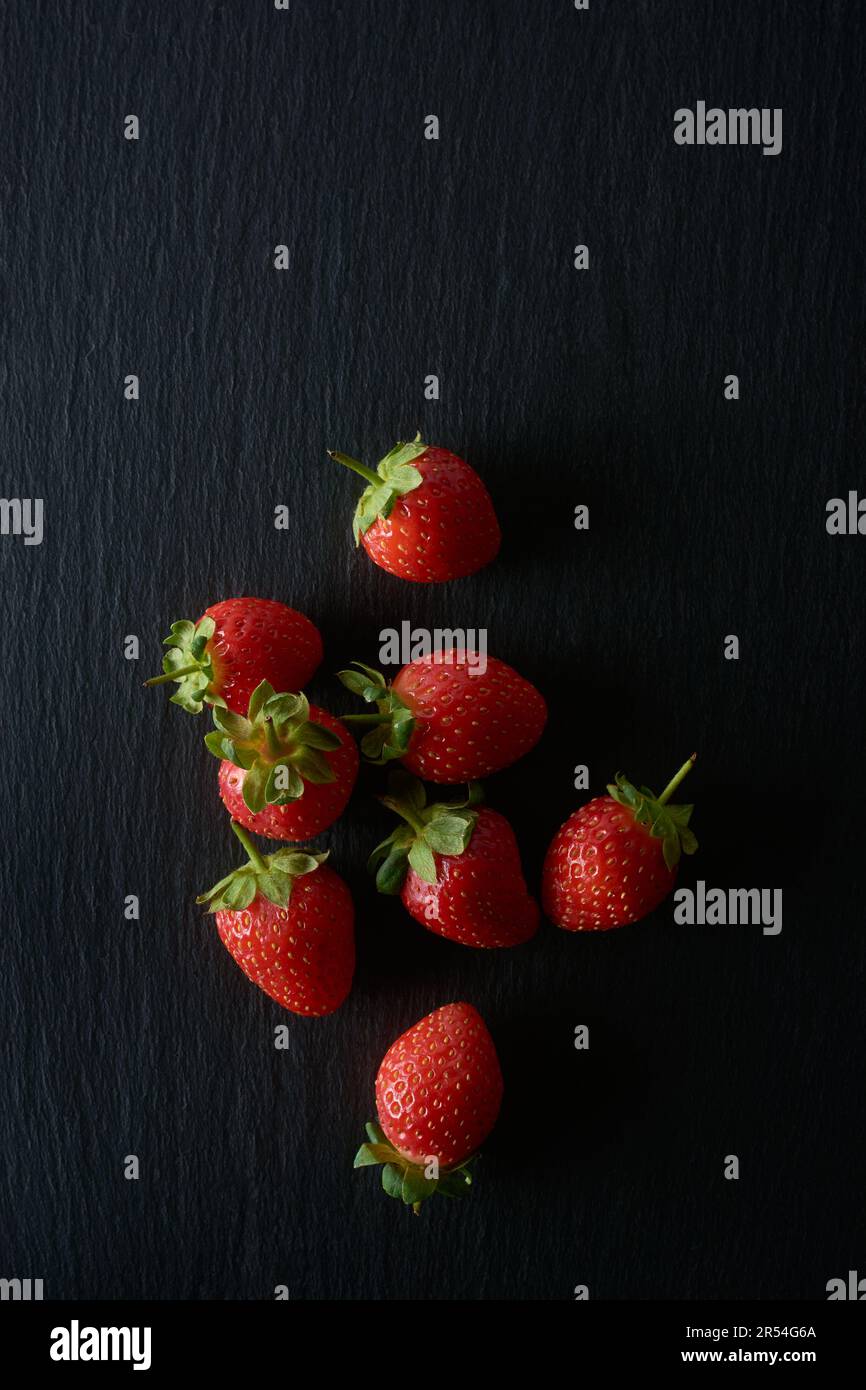 Erdbeeren auf schwarzem, strukturiertem Hintergrund, hellrote Farbe beliebte saftige Früchte mit süßem Geschmack und duftendem Aroma, gesund und sehr nahrhaft Stockfoto
