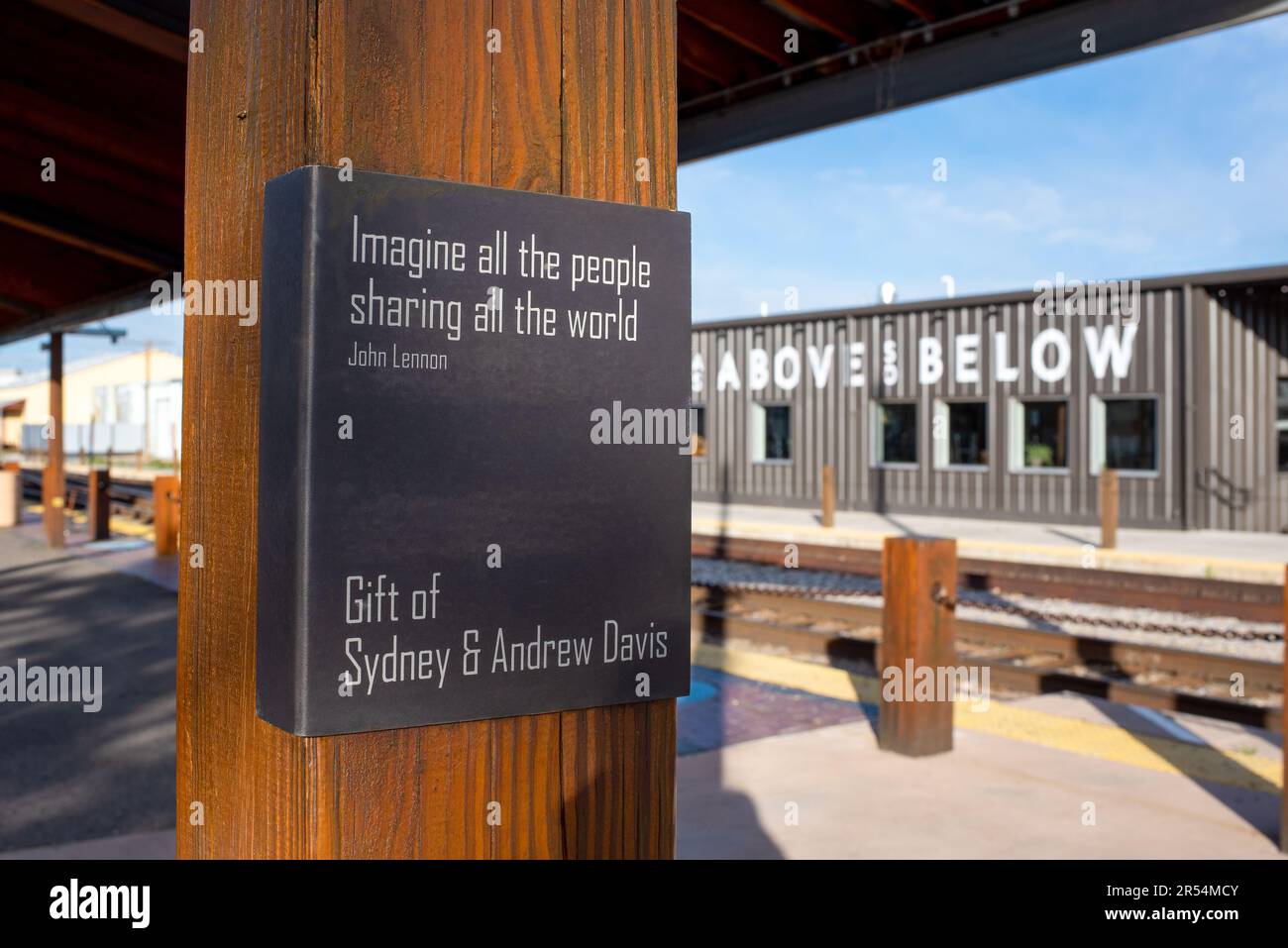 Eine quadratische Tafel auf einem Holzpfosten der Santa Fe Railyard mit einem Zitat von John Lennon: Stellen Sie sich vor, wie alle Menschen die Welt teilen. Stockfoto