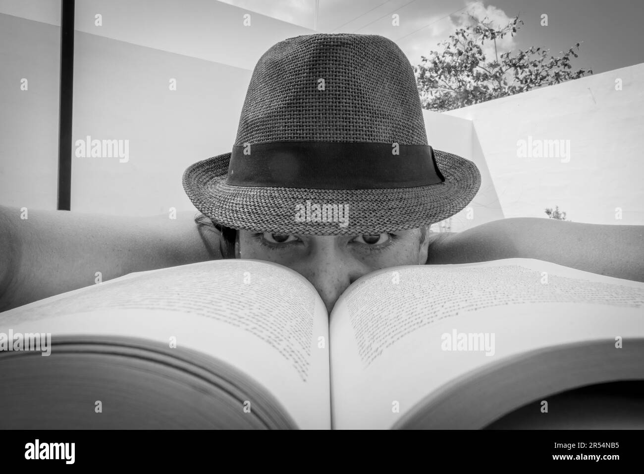 Eine Person mit Hut schaut über ein offenes Buch. Schwarzweißfoto Stockfoto