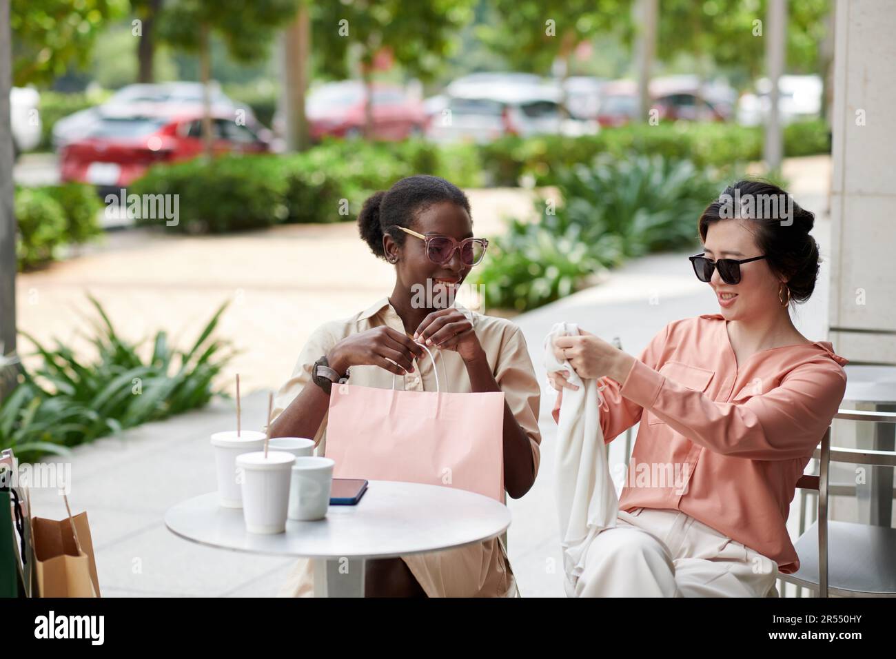 Frau zeigt ein neues Seidenoberteil, das sie im Angebot gekauft hat, als sie mit einem Freund im Café saß Stockfoto