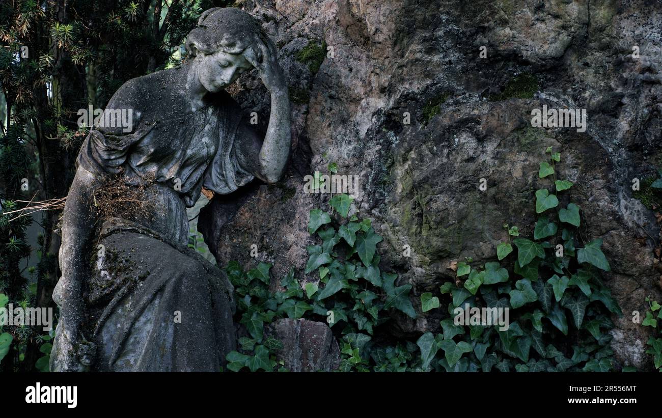 Skulptur einer schönen trauernden Frau auf einem Friedhof. Sie lehnt sich auf einen unangebrachten Stein. Stockfoto