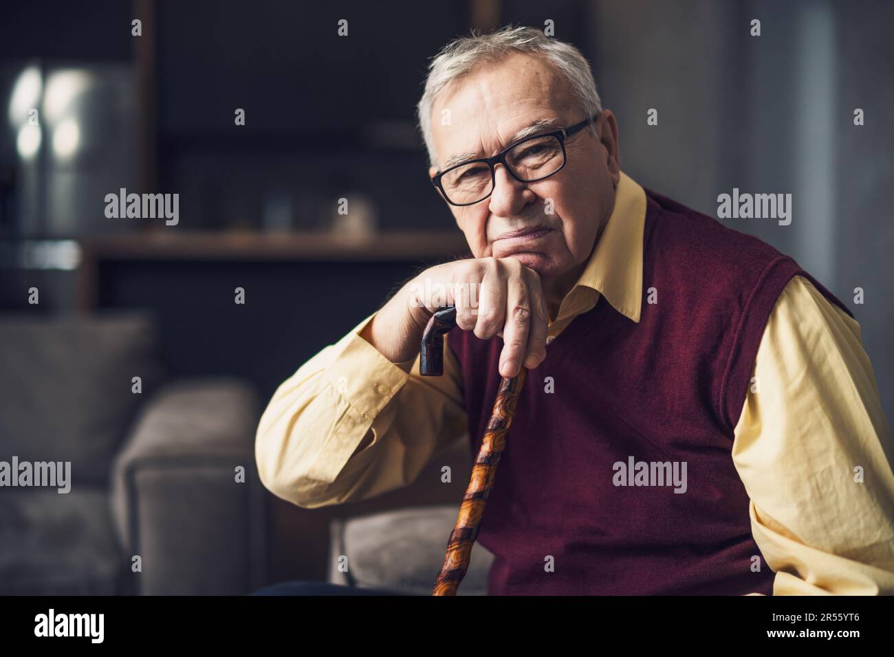 Ein nachdenklicher und besorgter Seniorenmann sitzt in seinem Haus auf dem Bett. Porträt eines Seniorenmannes mit Gehstock. Stockfoto