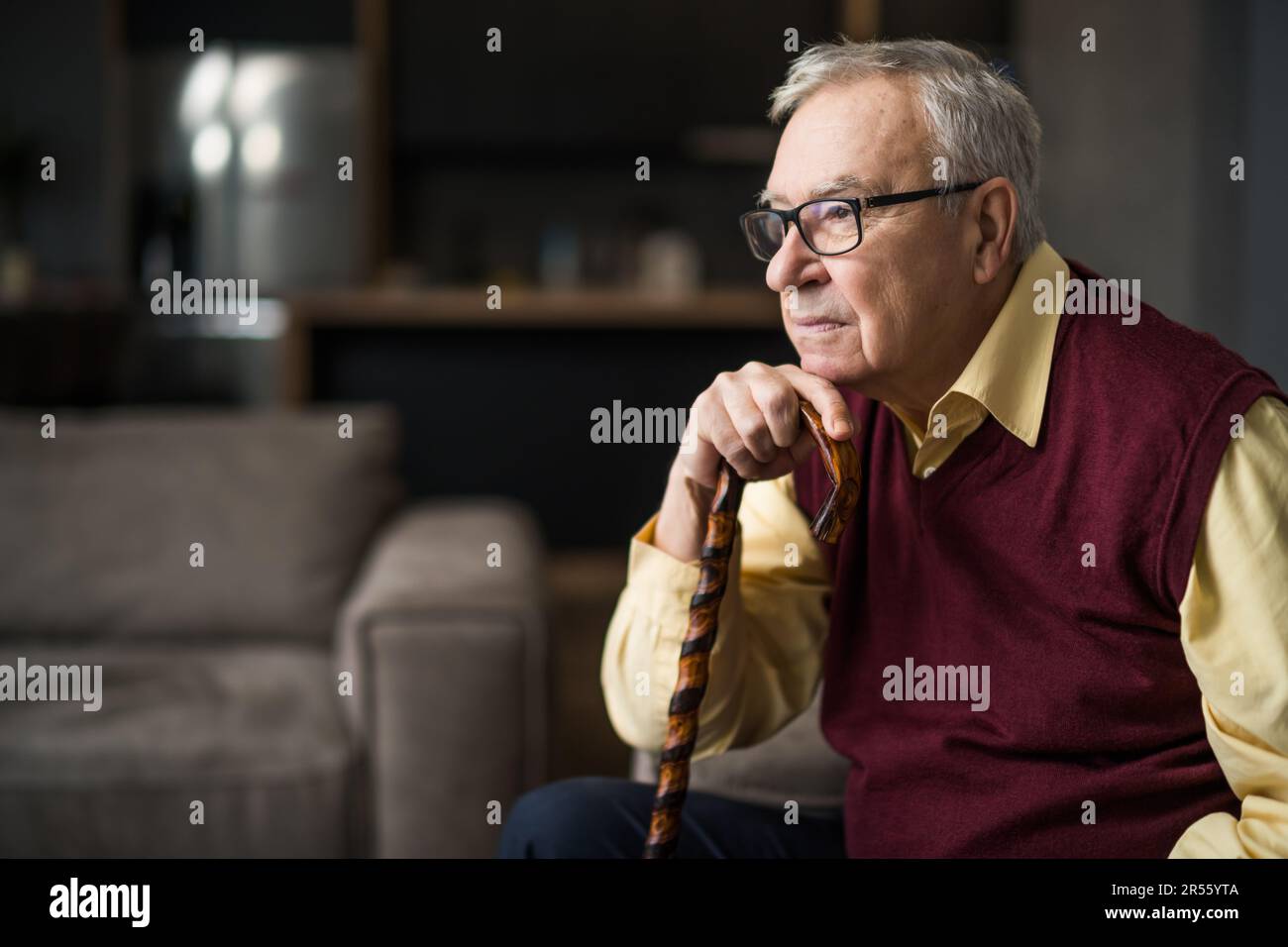 Ein nachdenklicher und besorgter Seniorenmann sitzt in seinem Haus auf dem Bett. Porträt eines Seniorenmannes mit Gehstock. Stockfoto