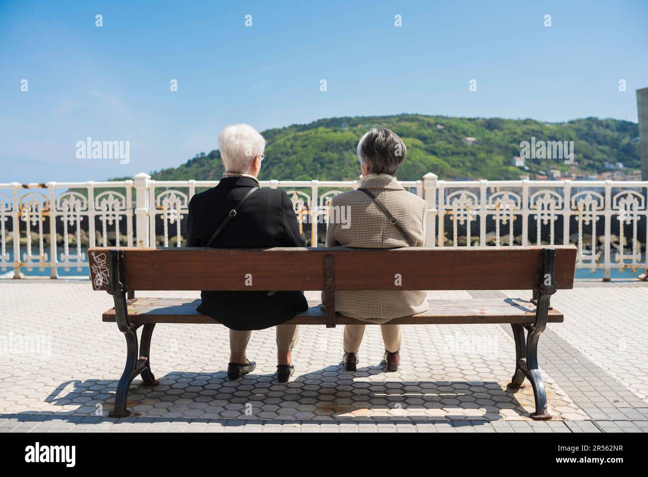 Weibliche Freunde, Rückblick auf zwei ältere weibliche Freunde, die sich auf einer Bank entlang der Promenade in San Sebastian - Donostia, Spanien unterhalten. Stockfoto
