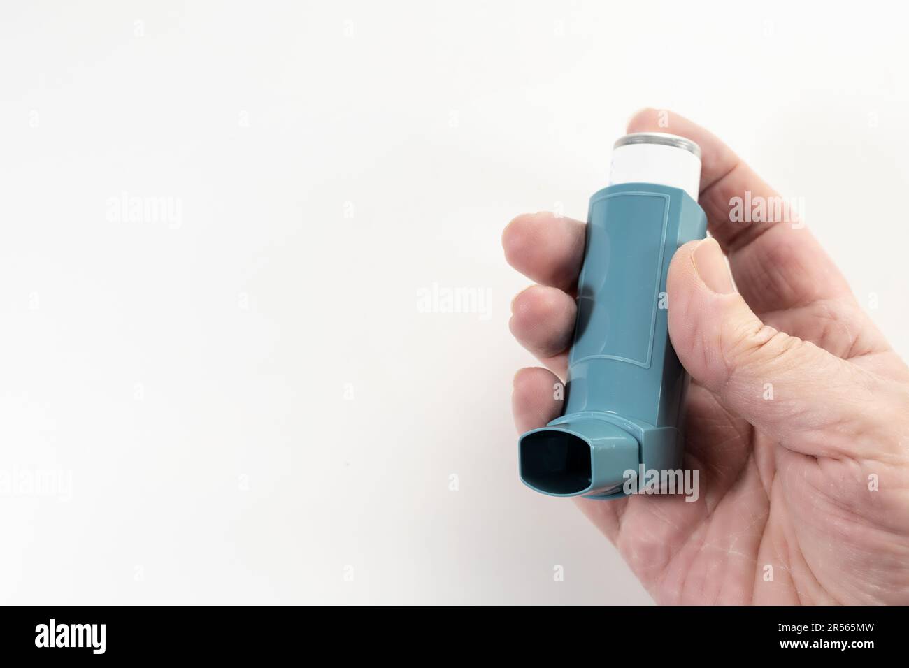 Hand hält einen blauen Inhalator, auch bekannt als Pumpe oder Allergie Spray, medizinisches Gerät für Asthma- oder COPD-Patienten, heller Hintergrund, großer Kopierraum, Sele Stockfoto