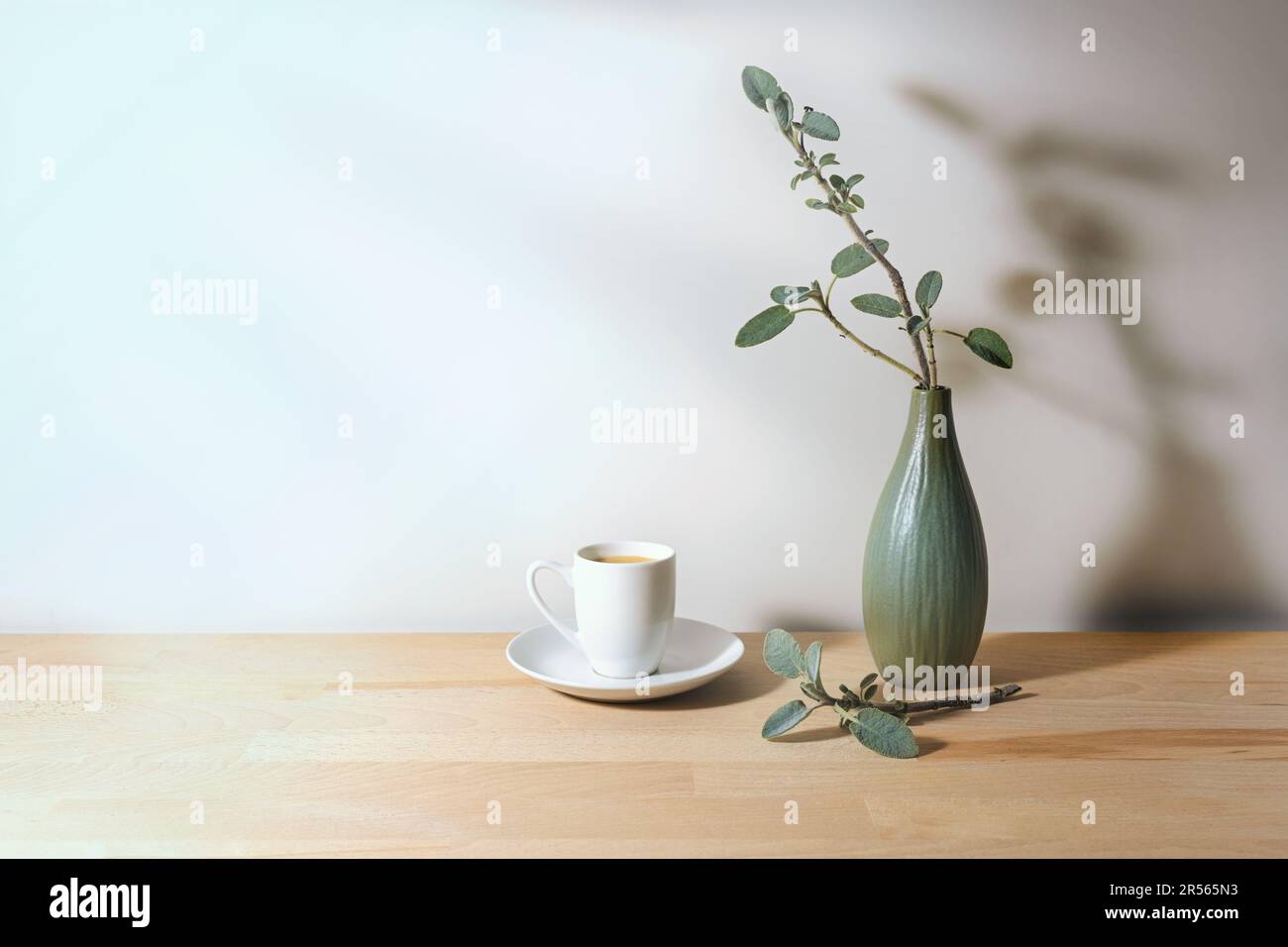 Kaffeetasse und graue grüne Vase mit Salbeizweigen auf einem Holztisch an einer hellen Wand in der Morgensonne, einfache Hausdekoration, Kopierraum, Sel Stockfoto