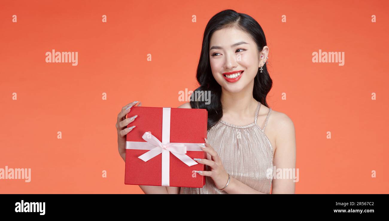 Ein junges Mädchen mit einem wunderschönen breiten Lächeln hält ein Überraschungsgeschenk für den Urlaub in der Hand Stockfoto