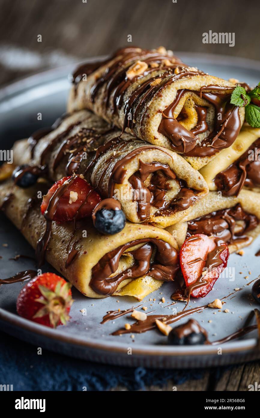 Crepes mit Schokoladenfüllung in Pyramidenform mit Erdbeeren der Saison, Kirschen und Blaubeeren auf einem rustikalen blauen Teller Stockfoto