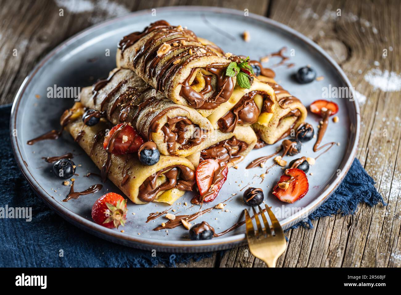 Crepes mit Schokoladenfüllung in Pyramidenform mit Erdbeeren der Saison, Kirschen und Blaubeeren auf einem rustikalen blauen Teller Stockfoto