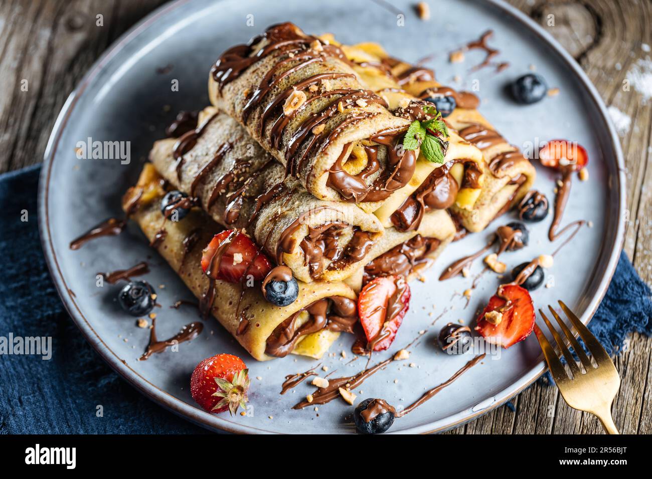 Crepes mit Schokoladenfüllung in Pyramidenform mit Erdbeeren der Saison, Kirschen und Blaubeeren auf einem rustikalen blauen Teller Stockfoto