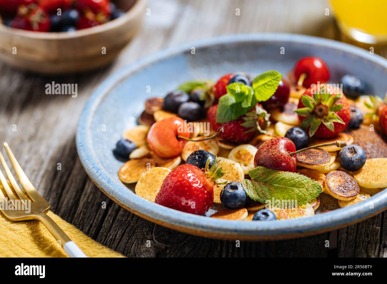 Kleine amerikanische Pfannkuchen mit Obst der Saison wie Erdbeeren, Heidelbeeren und Kirschen. Mit geschmolzener Schokolade getaucht, auf rustikalem Holz Stockfoto