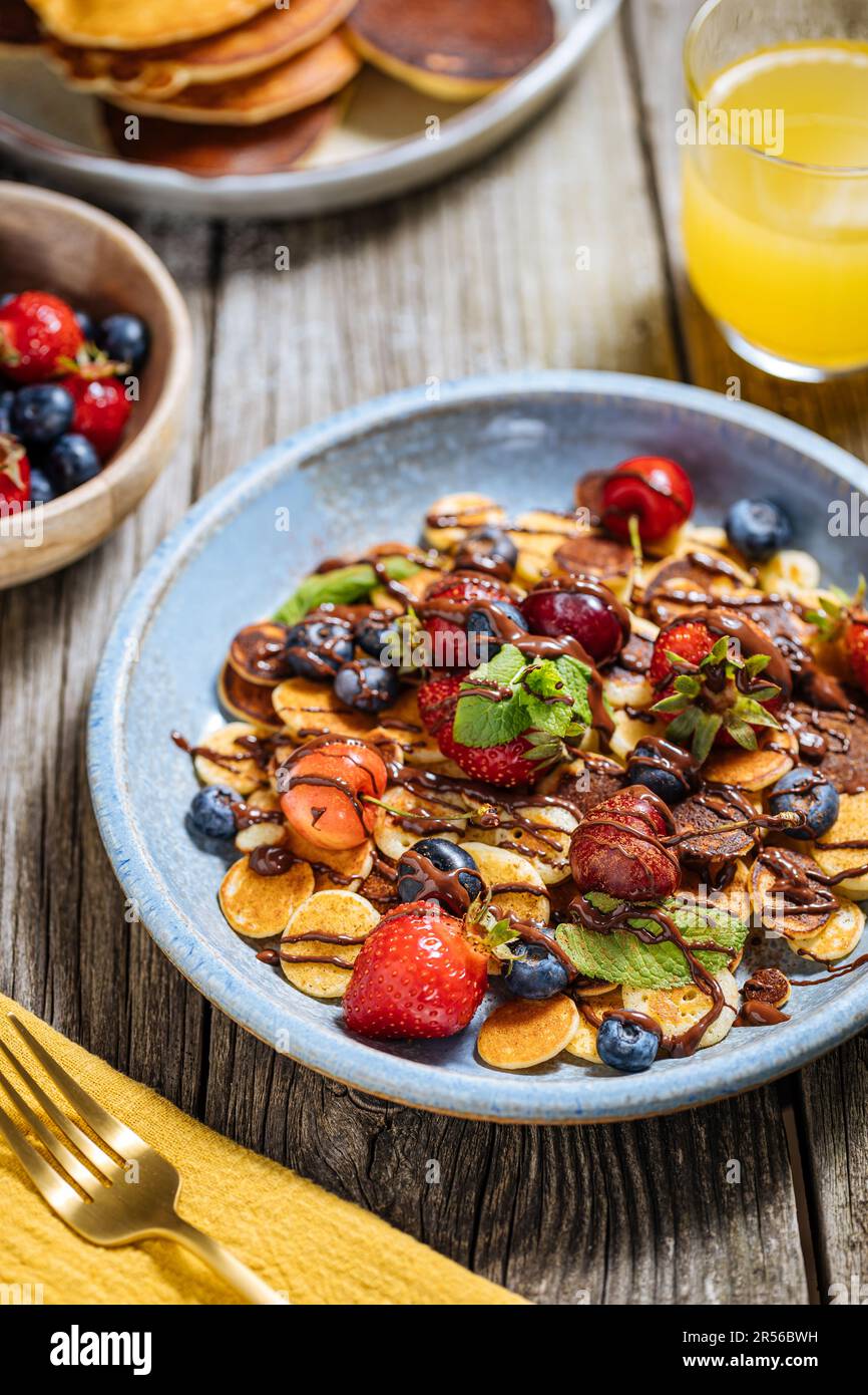 Kleine amerikanische Pfannkuchen mit Obst der Saison wie Erdbeeren, Heidelbeeren und Kirschen. Mit geschmolzener Schokolade getaucht, auf rustikalem Holz Stockfoto