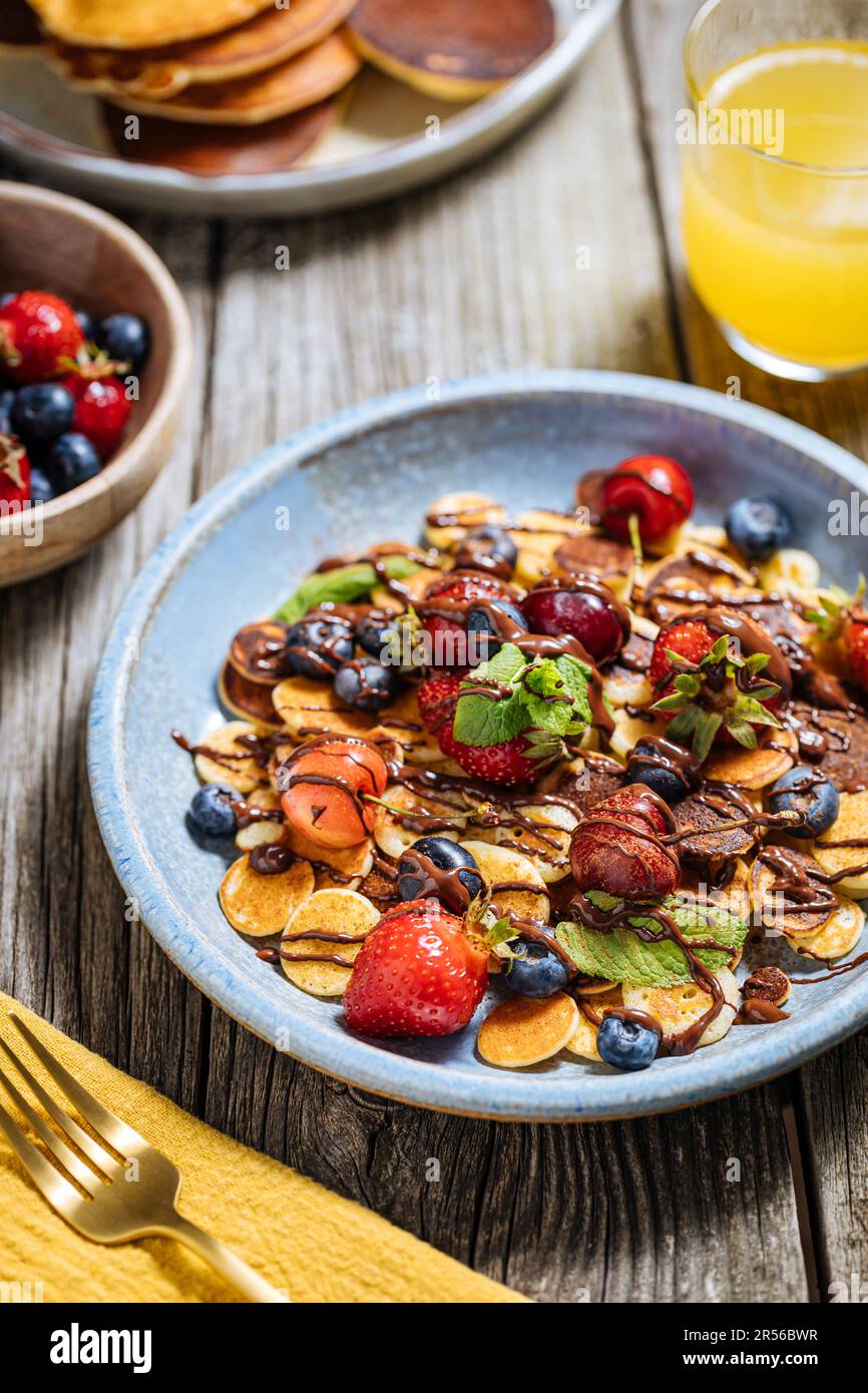 Kleine amerikanische Pfannkuchen mit Obst der Saison wie Erdbeeren, Heidelbeeren und Kirschen. Mit geschmolzener Schokolade getaucht, auf rustikalem Holz Stockfoto