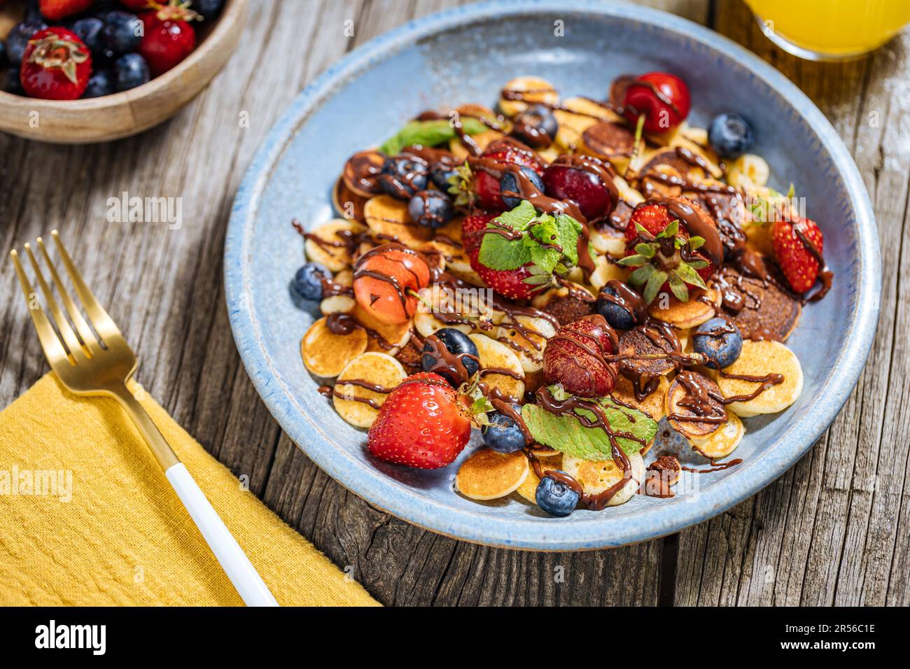 Kleine amerikanische Pfannkuchen mit Obst der Saison wie Erdbeeren, Heidelbeeren und Kirschen. Mit geschmolzener Schokolade getaucht, auf rustikalem Holz Stockfoto
