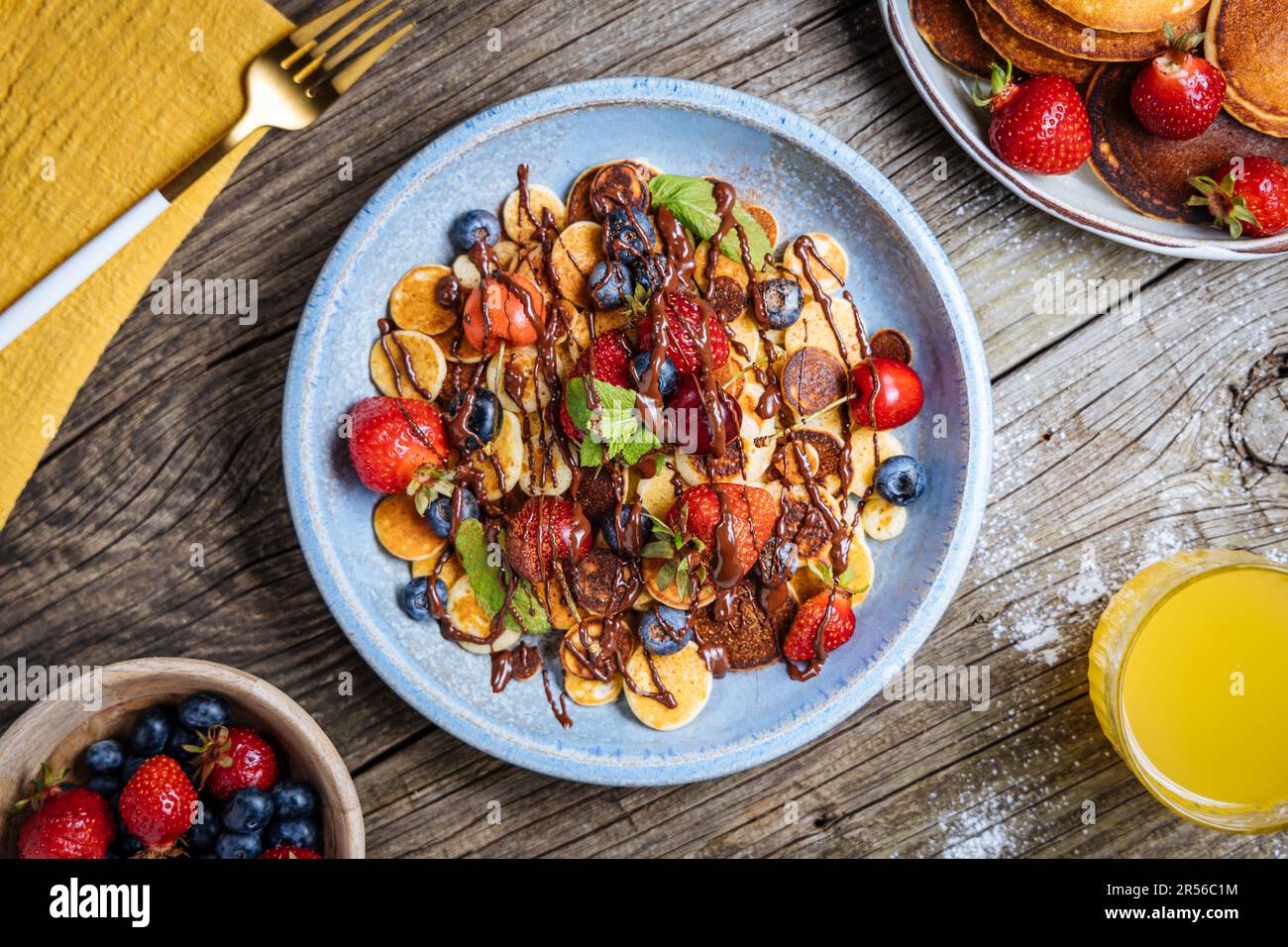 Kleine amerikanische Pfannkuchen mit Obst der Saison wie Erdbeeren, Heidelbeeren und Kirschen. Mit geschmolzener Schokolade getaucht, auf rustikalem Holz Stockfoto