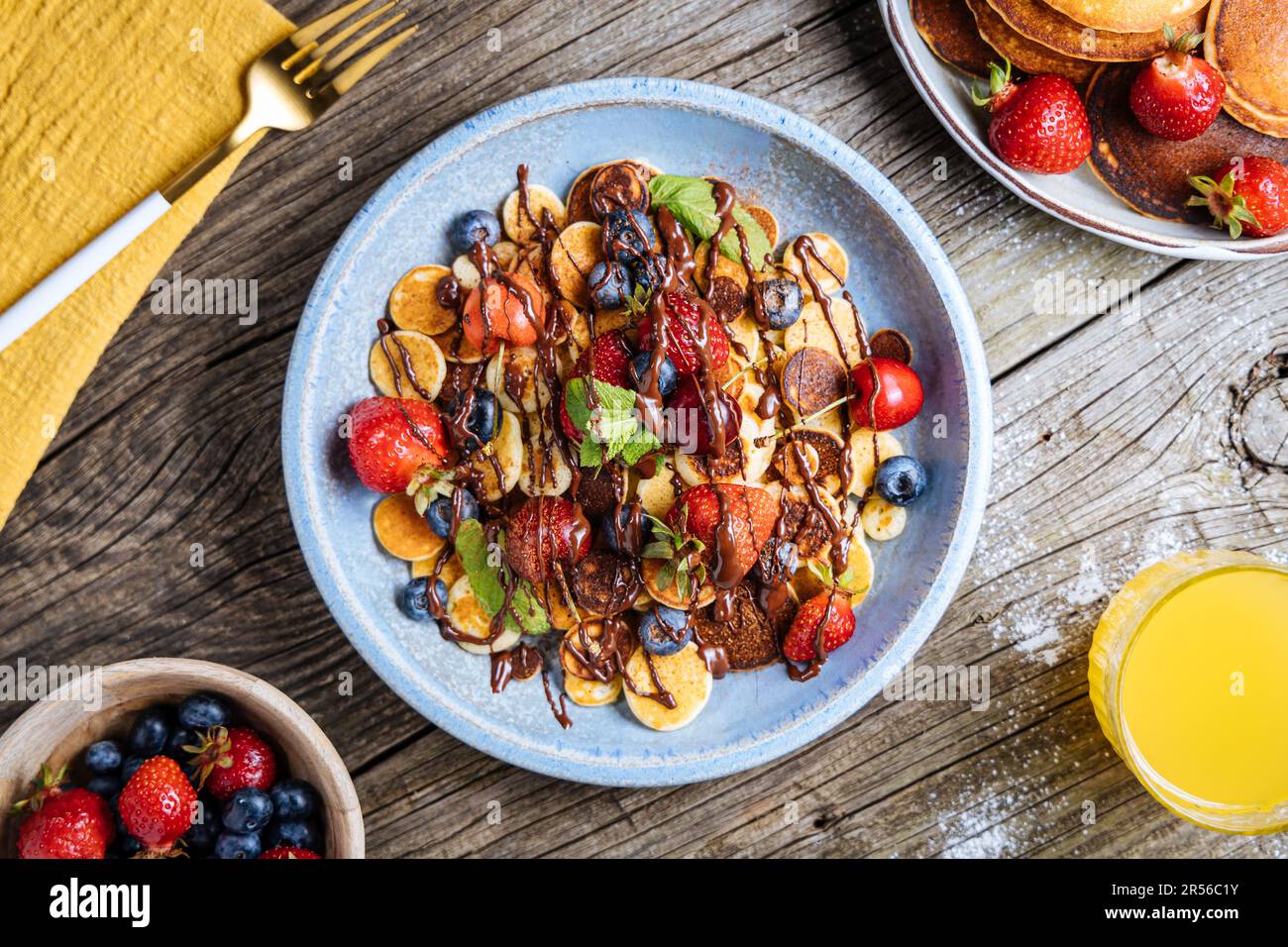 Kleine amerikanische Pfannkuchen mit Obst der Saison wie Erdbeeren, Heidelbeeren und Kirschen. Mit geschmolzener Schokolade getaucht, auf rustikalem Holz Stockfoto