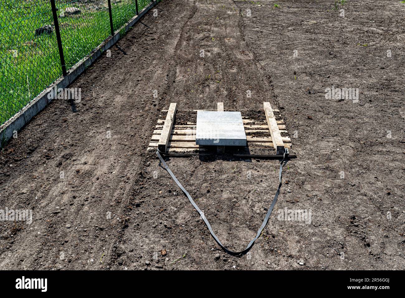 Nivellierung des Chernozem im Hof mit einer Palette, gewichtet mit einem Betonwürfel, Vorbereitung für die Aussaat des Rasens. Stockfoto