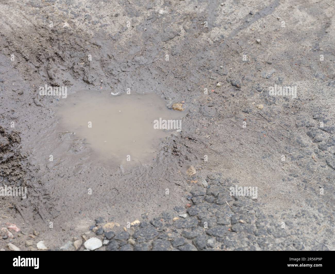 Nahaufnahme einer schlammigen Pfütze auf einer gerissenen Straße. Stockfoto