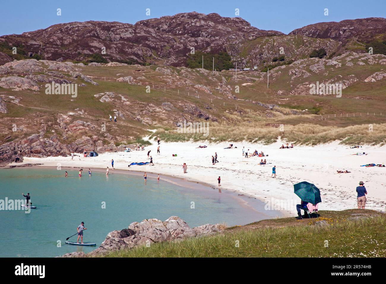 Achmelvich Bay, Assynt, Beach, North West Highlands, Schottland, UK. Juni 2023. Sonniger Nachmittag an der Westküste der schottischen Highlands Temperatur um 14 Grad Celsius. Mit Dutzenden von Menschen auf dem silbernen Sand, um den Blick auf den preisgekrönten Strand und die Wassersportmöglichkeiten auf der Minch zu genießen. Stockfoto