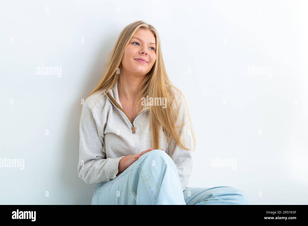 Porträt einer 19-jährigen blonden Frau, die sich vor weißem Hintergrund lehnt und wegblickt Stockfoto