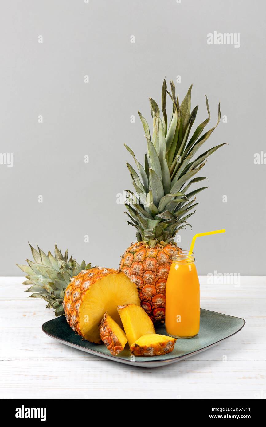 Scheiben saftiger Ananas und ein frischer, gesunder Smoothie in einer Glasflasche und ein Strohhalm auf einer grünen Platte auf Holzhintergrund. Gesund, Entgiftung und Dieta Stockfoto