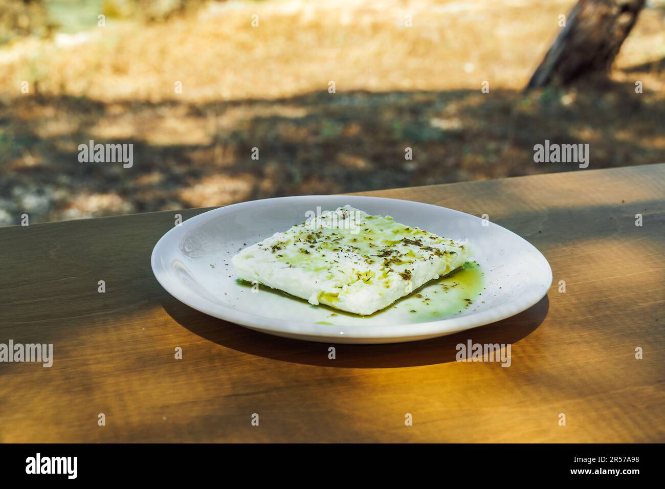 Eine Scheibe Feta-Weißkäse auf einem Holztisch im Freien serviert auf einem Gericht mit Oregano und Olivenöl. Stockfoto