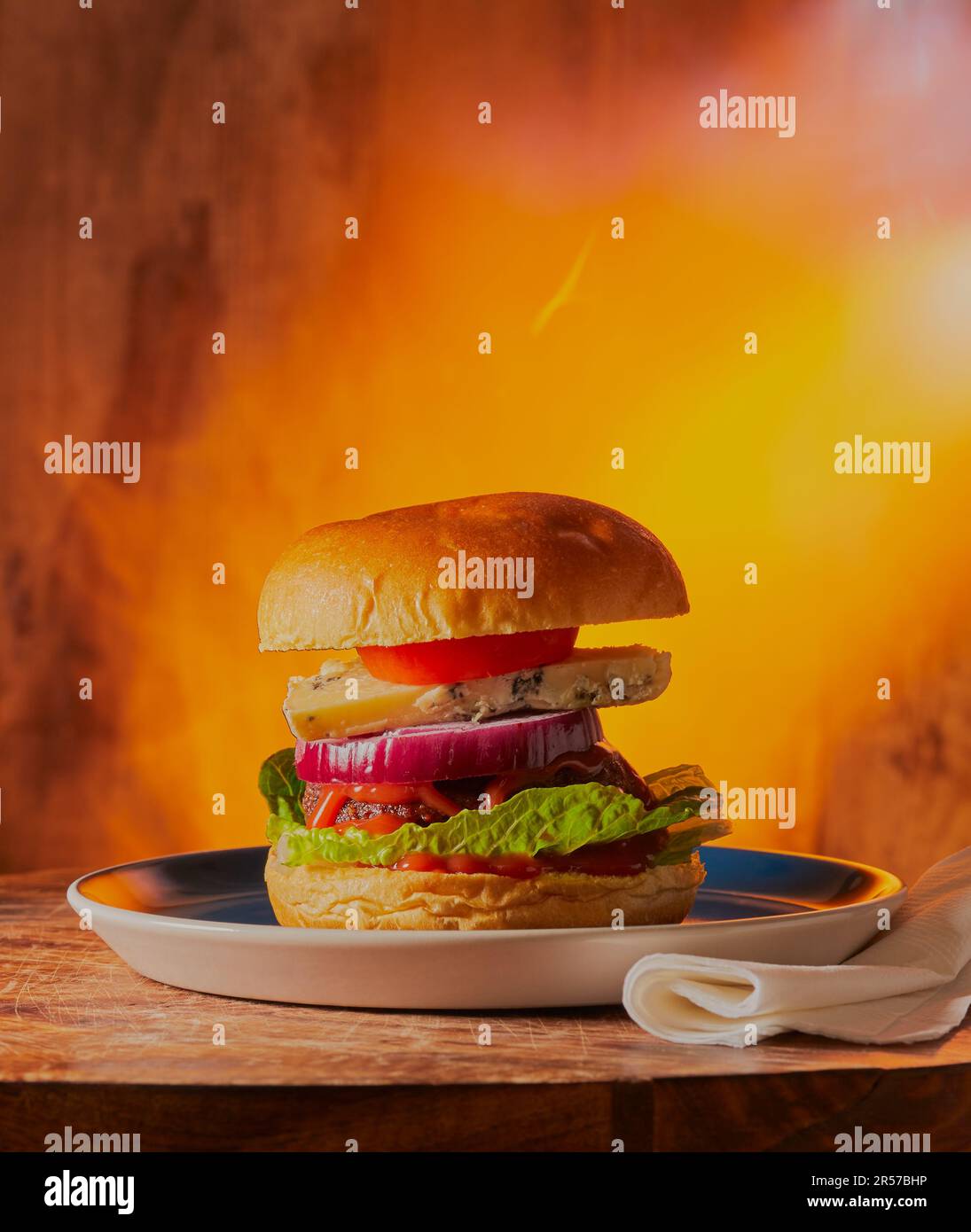 Mit Flammen gegrillter Käseburger auf einer Holzfläche mit Flammen hinter dem Burger. Stockfoto