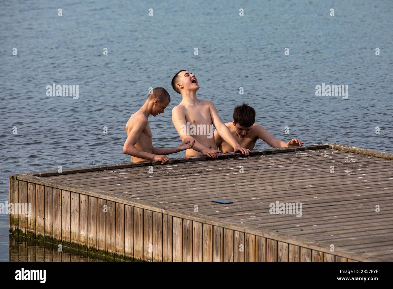 Teenager-Jungs stehen im kalten Wasser am Steg in der Bucht von Töölönlahti, Helsinki, Finnland Stockfoto