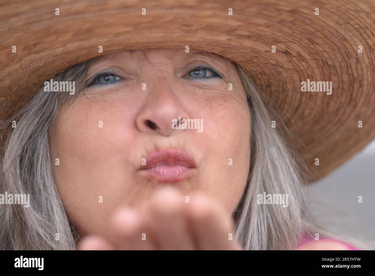 Nahaufnahme einer älteren Frau mit Hut, weißem Haar, blauen Augen und Sommersprossen, die einen Kuss in die Kamera bläst Stockfoto