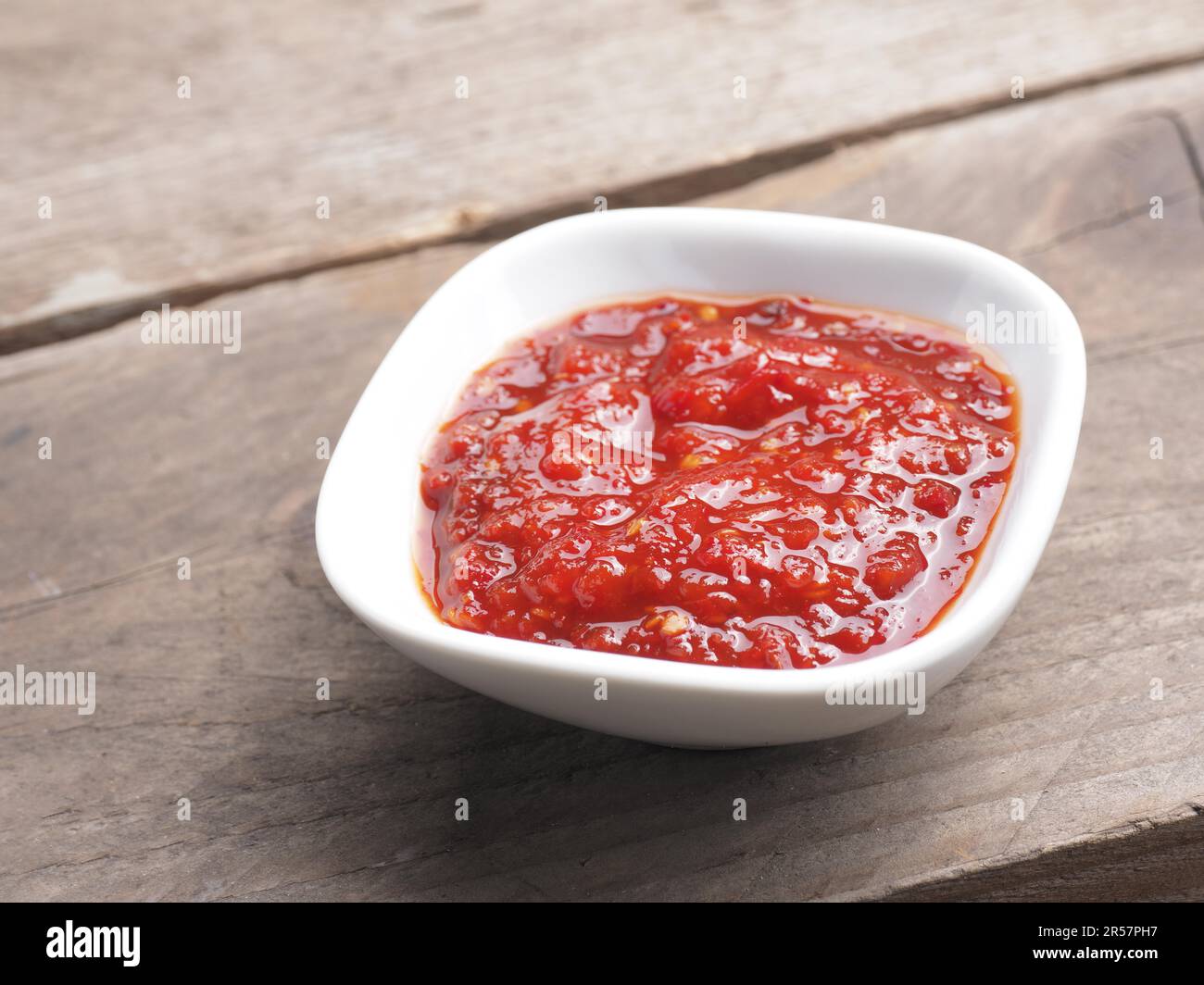 Sehr würzige Chilisauce in einer weißen Schüssel auf einem rustikalen Küchentisch aus Holz, Platz für Ihren Text Stockfoto